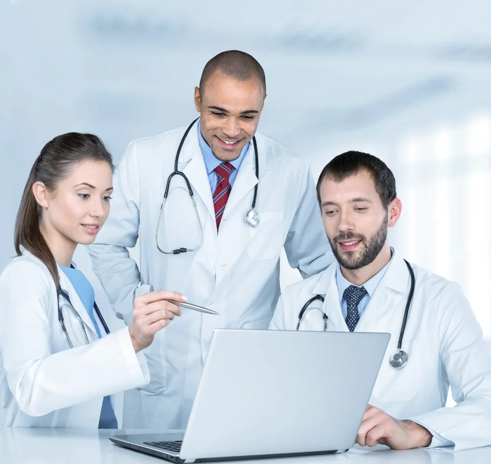 Three clinicians in white coats reviewing patient data on a laptop